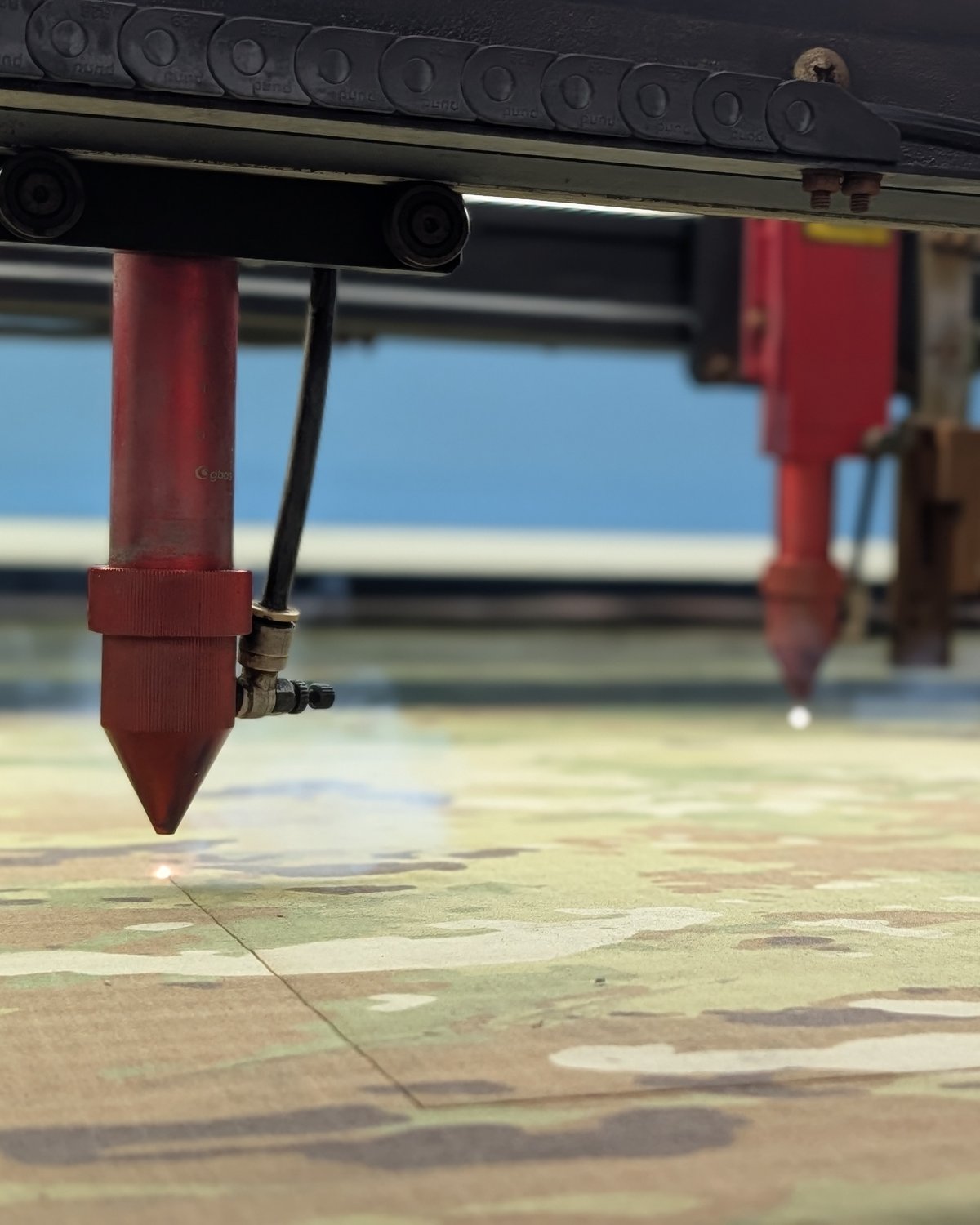 Dual-head laser cutter cutting camouflage fabric at Excel Manufacturing